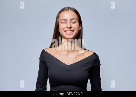 Jeune femme riante aux yeux fermés souriant sur un fond gris en studio Banque D'Images