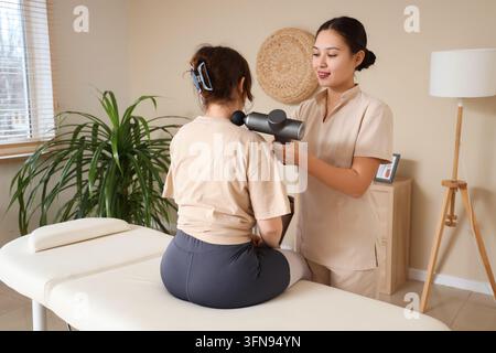 Thérapie physique et récupération musculaire, thérapeute professionnel utilisant une pistolet de massage sur l'épaule du patient pour soulager la douleur et réhabiliter les blessures sportives Banque D'Images