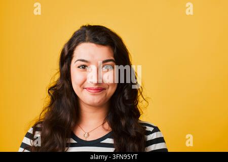Portrait souriant d'une jeune femme avec fond jaune portant une chemise rayée et un collier Banque D'Images