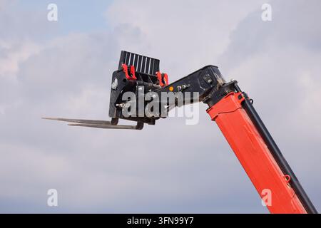 Grossissement du bras télescopique rouge et du bras de levage hydraulique avec les fourches à palette relevées contre un ciel nuageux sur le chantier. Banque D'Images