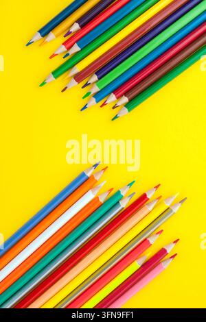 Crayons de couleur disposés sur un fond jaune vif, créant une composition vibrante pour l'art, le dessin, la créativité, l'éducation et les fournitures scolaires Banque D'Images