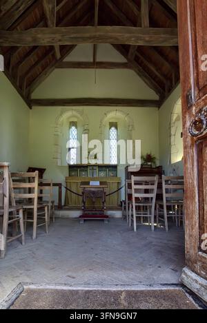 L'intérieur minuscule de l'église de Lullington dans l'East Sussex, montrant des poutres en bois, des chaises en bois simples et l'autel vu à travers l'entrée ouverte. Banque D'Images
