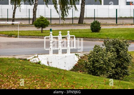 Une structure de grille de drainage en métal blanc est posée sur une pelouse verte paysagée à côté d'une route asphaltée en extérieur. La vue large met en évidence l'infrastructure municipale Banque D'Images