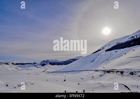 Vue des plaines et montagnes enneigées de Castelluccio sous un soleil éclatant avec un halo visible dans le ciel d'hiver à Castelluccio, Ombrie, Italie. Banque D'Images