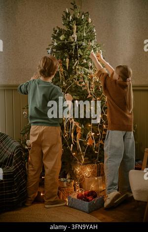 Enfants décorant ensemble le sapin de Noël à la maison Banque D'Images
