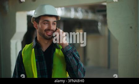 Homme caucasien joyeux parlant au téléphone portable, ouvrier d'usine, maçon appréciant la conversation, bricoleur, travailleur souriant, entrepreneur passant un appel sur smartphone Banque D'Images