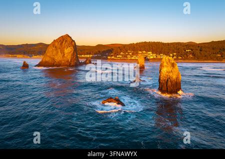Une vue aérienne à couper le souffle sur Haystack Rock et la côte de Cannon Beach, baignée par la lumière chaude et dorée d'un coucher de soleil vibrant sur l'océan Pacifique Banque D'Images
