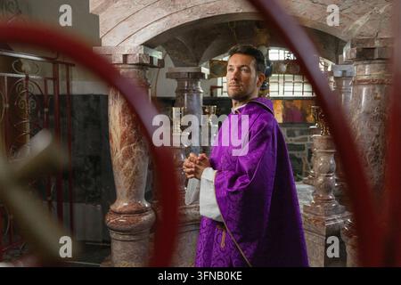 Un prêtre catholique se tient dans une église prêt à célébrer une messe solennelle, vêtu de paraments liturgiques. Le cadre comprend des symboles religieux. Banque D'Images