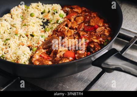 Riz avec légumes et viande dans une sauce tomate servi dans une poêle noire. Fond de dîner fait maison pour un repas copieux, la cuisine et la nourriture réconfortante savoureuse. Banque D'Images