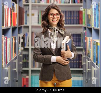 Bibliothécaire posant dans une bibliothèque devant des étagères de livres Banque D'Images