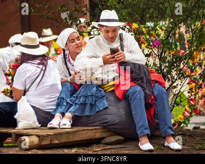 Un jeune couple en tenue traditionnelle colombienne assis sur un banc en bois pendant une pause à la Feria de las Flores Banque D'Images