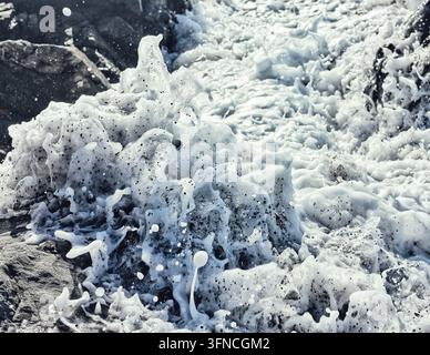 Prise de vue rapprochée d'action de vagues agitées de l'océan éclaboussant de l'écume et des embruns contre les rochers côtiers Banque D'Images