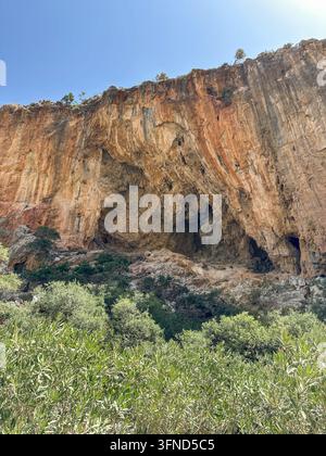 Falaise dramatique érodée avec une grande grotte naturelle s'élevant au-dessus d'une végétation méditerranéenne dense, créant un paysage sauvage frappant pour la géologie, a Banque D'Images