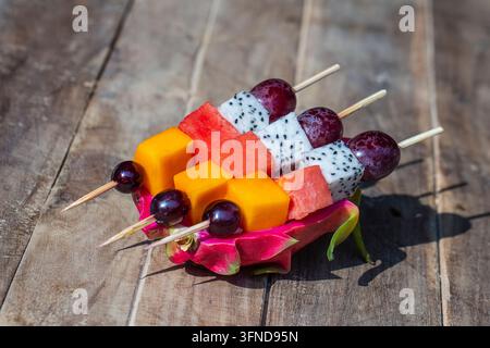 Fruits tropicaux frais – raisins, mangue, pastèque et pitahaya sur des brochettes dans une assiette blanche – petit-déjeuner sain, concept de perte de poids. Thaïlande. Gros plan Banque D'Images