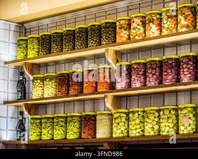 Verres remplis d'olives, de poivrons marinés, d'ail et de légumes variés conservés, exposés sur des étagères en bois à l'intérieur de la boutique de pâtes italiennes Bigoi. Banque D'Images