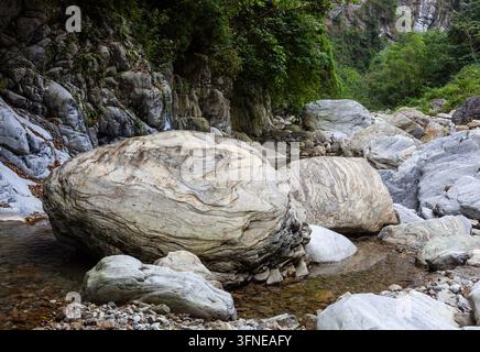 Des rochers de marbre à motifs reposent dans un lit de rivière. Des falaises verdoyantes entourent la vallée de Sanzhanxi à Taroko, à Taïwan. Une eau claire coule sur les pierres. Banque D'Images