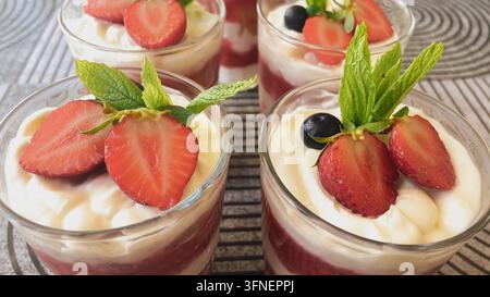 Vue rapprochée de desserts tiramisu aux fraises sans œufs portionnés dans des verres, décorés de tranches de baies fraîches, de feuilles de menthe et d'une crème riche au mascarpone. Banque D'Images