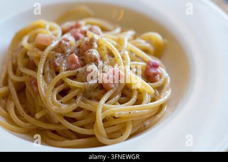 Close-up de spaghettis alla gricia enroulés dans un bol blanc avec du guanciale coupé en dés, du poivre noir concassé et une sauce crémeuse au pecorino, lumière douce de la fenêtre Banque D'Images