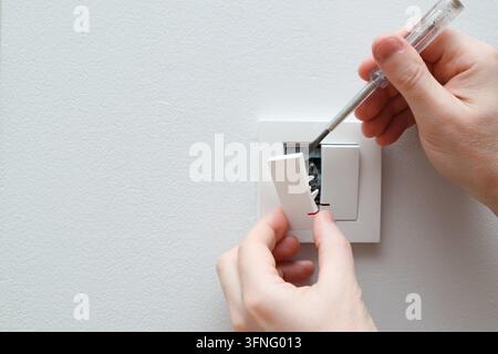 Un électricien remplace un interrupteur mural. Un concept de projet DIY. Danger de haute tension. Électricien réparant le panneau de commande de l'éclairage mural. Banque D'Images
