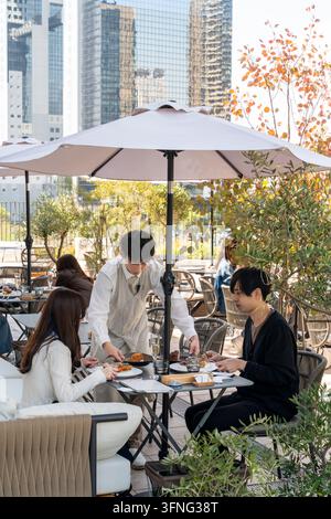 Serveur servant à un jeune couple profitant d'un repas dans un restaurant en toit-terrasse sur la terrasse du bâtiment Umekita Green Place. Banque D'Images
