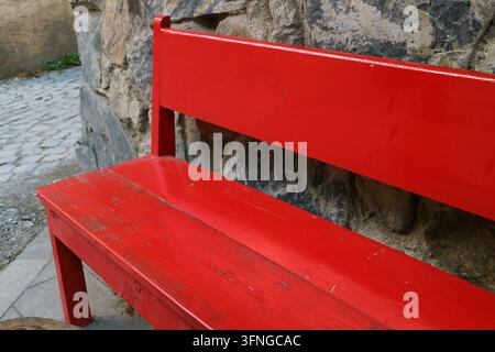 Gros plan d'un banc peint en rouge vide à côté d'un vieux mur texturé en pierre Banque D'Images