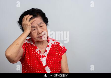 Sénior asiatique déprimée, seule, déçue et perdant sa mémoire sur un fond blanc isolé. Portrait d'une vieille femme malade, souffrant de dépression, de maladie, se sent triste Banque D'Images