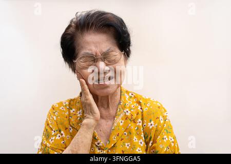 Ancienne femme asiatique souffrant d'une forte douleur dentaire, tenant sa joue et souffrant d'une forte douleur dentaire sur fond blanc, carie, sensibilité dentaire Banque D'Images