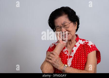 Ancienne femme asiatique souffrant d'une forte douleur dentaire, tenant sa joue et souffrant d'une forte douleur dentaire sur fond blanc, carie, sensibilité dentaire Banque D'Images
