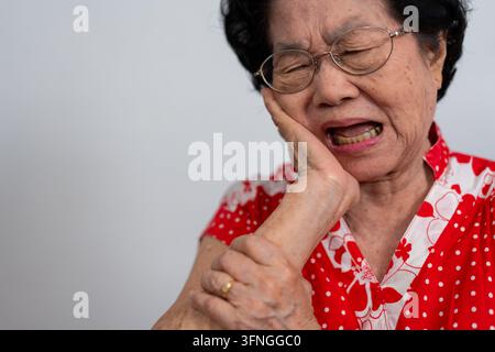 Ancienne femme asiatique souffrant d'une forte douleur dentaire, tenant sa joue et souffrant d'une forte douleur dentaire sur fond blanc, carie, sensibilité dentaire Banque D'Images