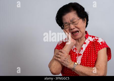 Ancienne femme asiatique souffrant d'une forte douleur dentaire, tenant sa joue et souffrant d'une forte douleur dentaire sur fond blanc, carie, sensibilité dentaire Banque D'Images