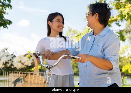 Lien générationnel, une scène réconfortante d'une fille adulte et de sa mère partageant un moment tendre en plein air, avec un vélo orné de fleurs en t Banque D'Images