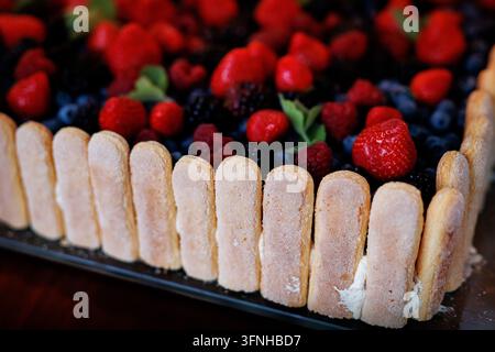 Prise détaillée d'un gâteau festif aux baies entouré de biscuits à la cuillère et chargé de fraises et de mûres fraîches. Banque D'Images