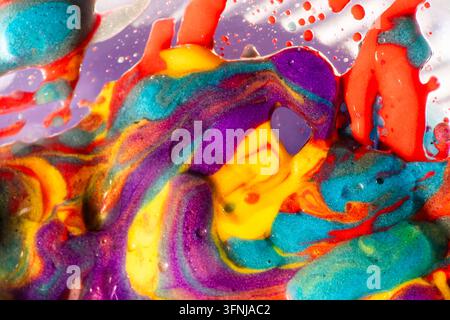 Photographie macro vibrante de peinture jaune, violette, turquoise et rouge tourbillonnante avec des bulles brillantes, créant un fond abstrait énergique avec une richesse Banque D'Images