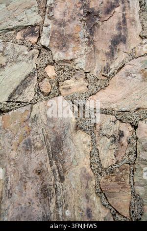 Image de fond verticale d'un mur en pierre naturelle rustique présentant des dalles d'ardoise multicolores jointes avec un mortier sablonneux. Banque D'Images
