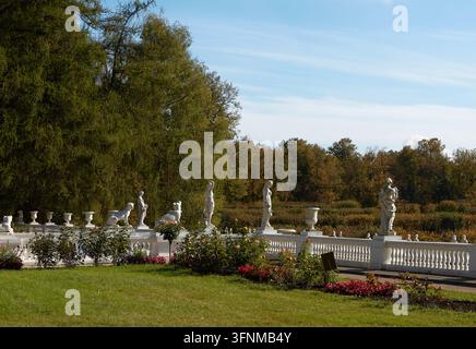 Des statues en pierre et des urnes bordent une balustrade blanche au-dessus de parterres de fleurs formels, de haies taillées, de pelouse et d'arbres matures sous un ciel bleu Banque D'Images