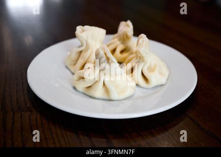 Dumplings khinkali bouillis servis sur une assiette blanche ronde, portion de cuisine géorgienne traditionnelle sur un fond de table en bois sombre de restaurant, chaud et savoureux Banque D'Images