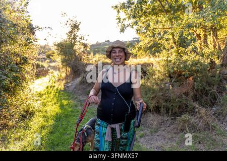 Femme enceinte heureuse profitant d'une promenade avec son chien dans la nature, embrassant la maternité et un mode de vie sain Banque D'Images