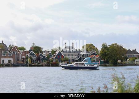 Zaanse Schans, Pays-Bas – 1er octobre 2026 : Des maisons et des bateaux traditionnels en bois vert bordent la rivière Zaan sous un ciel nuageux. Banque D'Images