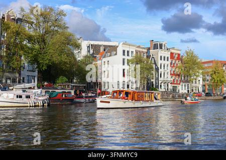 Amsterdam, Pays-Bas - 1er octobre 2026 : Un bateau traditionnel en bois transporte des touristes le long d'immeubles élégants du front de mer. Banque D'Images