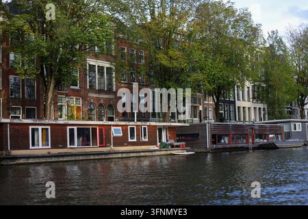 Amsterdam, Pays-Bas – 1er octobre 2026 : des bateaux de passagers partagent le canal à côté des embarcations amarrées et de l'architecture néerlandaise classique. Banque D'Images