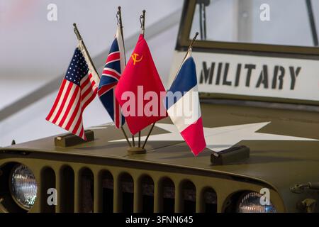 VIENNE, AUTRICHE, 26 octobre 2025 : Un véhicule militaire miniature est présenté avec quatre drapeaux nationaux et un signe militaire. Banque D'Images