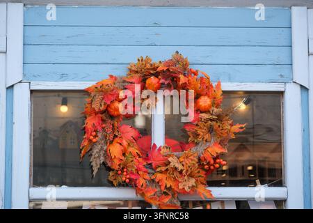 Une couronne d'automne colorée décore une fenêtre en bois bleue au-dessus d'une vitrine de magasin. Banque D'Images