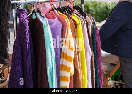 Des pulls et écharpes colorés sont suspendus en rangée sur un marché de vêtements en plein air. Banque D'Images