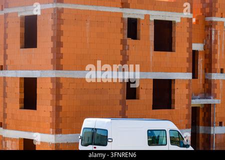 Camion de service blanc garé devant un immeuble résidentiel à plusieurs étages en construction avec des murs en briques rouges. Mise au point sélective. Banque D'Images