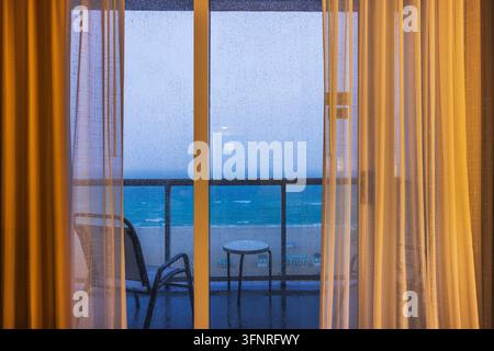 Vue magnifique sur l'océan Atlantique à travers les portes du balcon recouvertes de pluie, encadrées par des rideaux doucement éclairés. Miami Beach. États-Unis. Banque D'Images