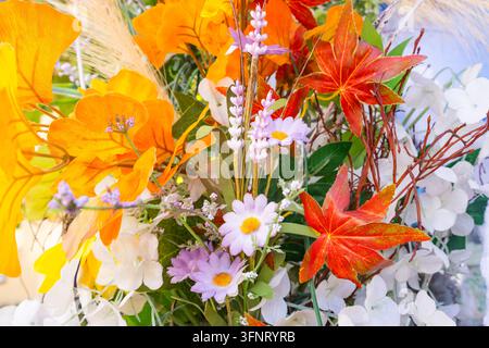 Décoration de bouquet d'automne lumineux avec des feuilles d'érable rouges artificielles, des feuillages orange, des marguerites lilas et des fleurs blanches en gros plan Banque D'Images
