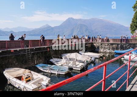 Varenna, Italie – 5 avril 2026 : Plusieurs petits bateaux amarrés dans un port paisible au bord du lac avec des touristes et des gens qui se promènent Banque D'Images