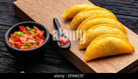 Empanadas colombiennes dorées et croustillantes servies sur une planche en bois avec de la tomate et de l'ají à l'oignon. Banque D'Images