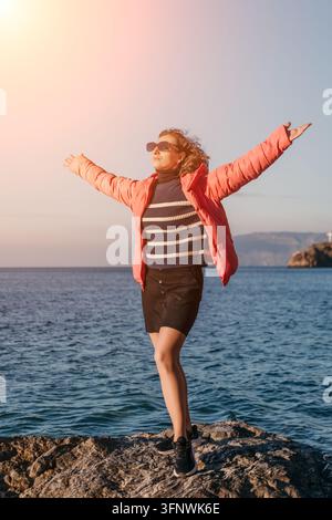 Femme liberté mer femme heureuse debout sur des rochers au bord de l'océan les bras grands ouverts profitant du soleil et de la brise Banque D'Images