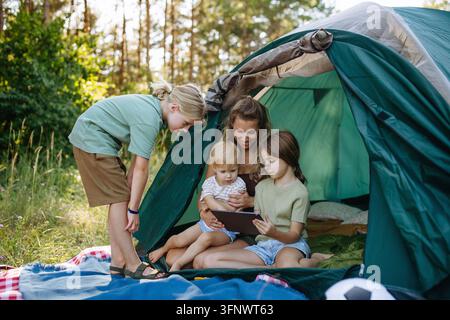 Mère et enfants utilisant une tablette ensemble lors d'un voyage de camping en famille. Banque D'Images